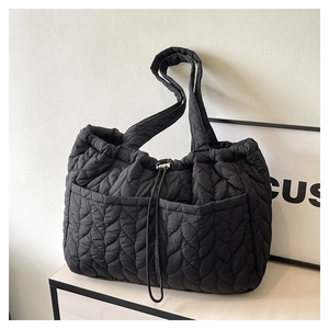 Detail of black quilted tote bag showing leaf-pattern stitching and side pockets