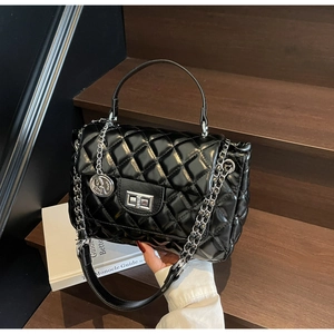 Detail of black quilted leather handbag with silver chain strap and metal lock closure