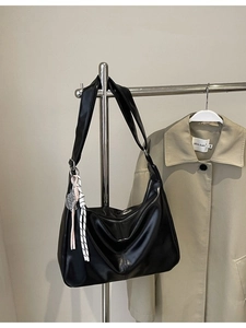 Minimalist black faux leather hobo bag with wide strap and tennis racket charm detail