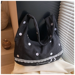 Détail d'un cabas en toile noire à pois blancs avec bordure en dentelle et petit nœud