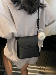 Chic black litchi pattern bucket bag with cute plush pendant on a model in sunlight