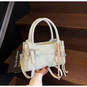 Dettaglio della borsa a mano con fiocco decorativo, ciondolo intrecciato e tracolla su scale
