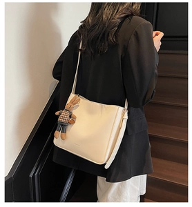 Détail du sac seau en cuir beige avec charm en peluche et logo de marque embossé sur le côté