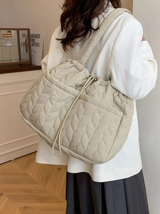 Beige quilted tote bag with leaf pattern and drawstring closure shown on model