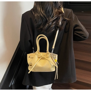 Detail der beigen Falten-Beuteltasche mit Schleife und Quaste auf schwarzem Blazer