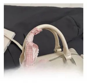 Detail of cream Boston bag handle with pink lace ribbon and silver heart charm decoration