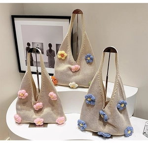 Three knitted floral tote bags displayed on white pedestals with metal stands
