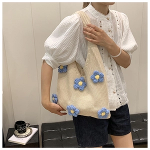 Detail of a beige knitted tote bag with blue 3D crochet flowers and wide shoulder straps