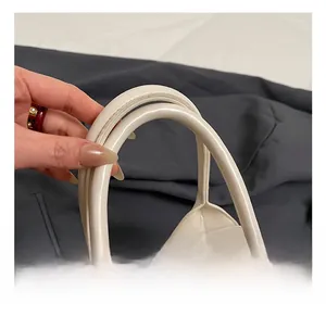 Macro detail of creamy white leather handbag featuring a smooth curved handle and stitching