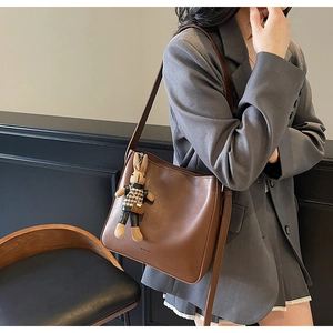 Détail du sac seau en cuir marron avec un pendentif lapin pied-de-poule sur la bandoulière