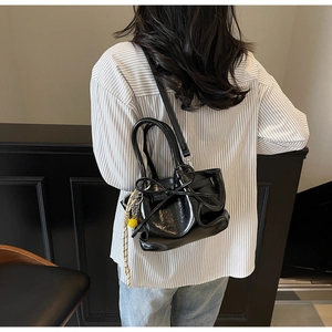 Detail der schwarzen Plissee-Eimertasche mit Schleife und gelbem Bommel am Model-Outfit