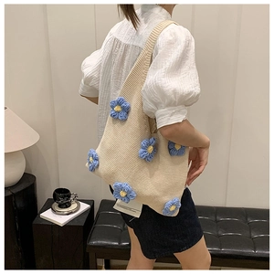 Close-up of cream knit tote bag with 3D blue floral accents worn on the shoulder
