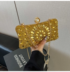 Détail de la pochette de soirée dorée avec motif floral en strass et fermoir perle