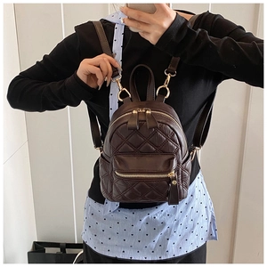 Detail eines dunkelbraunen Mini-Rucksacks mit Steppmuster und goldenen Reißverschlüssen