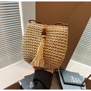 Dettaglio borsa a secchiello in paglia intrecciata a mano con nappe in legno e tracolla