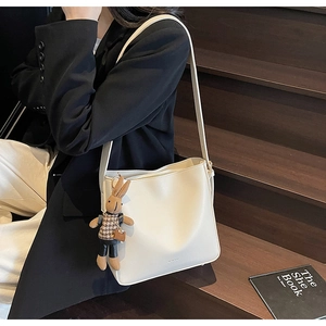 Détail du sac seau minimaliste blanc cassé avec breloque lapin sur un escalier en bois