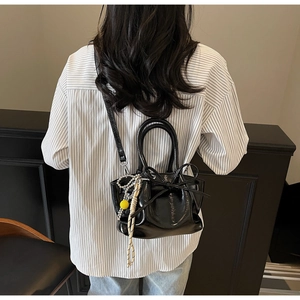 Detailansicht einer schwarzen glänzenden Plissee-Beuteltasche mit Schleife und Perle