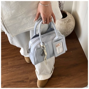 Close-up of light blue patent leather handbag with charm tag and woven rope detail