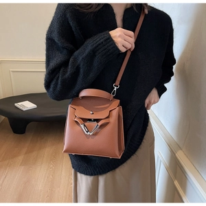 Detail einer braunen Handtasche mit Litschi-Muster und silbernem Dreiecksbeschlag