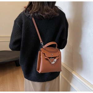 Rückansicht braune Handtasche aus Leder mit Litschi-Muster getragen von Modell in Schwarz