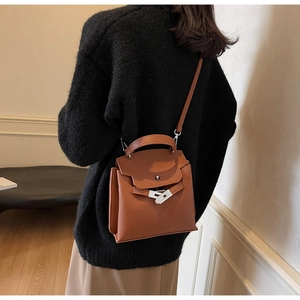 Braune Trapez-Handtasche aus Leder mit silbernem Drehverschluss auf schwarzem Pullover