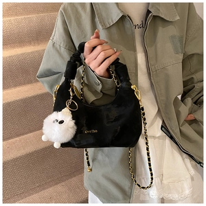 Gros plan du sac croissant en velours noir avec logo doré, anse plissée et peluche