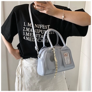 Detail of light blue patent leather pillow bag with woven tassel and metallic accents