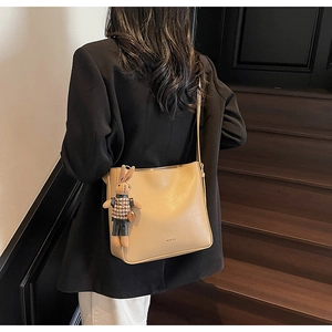 Détail d'un sac seau en cuir mat beige avec un pendentif lapin mignon sur la bandoulière