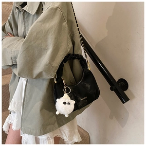 Detail of black pleated dumpling bag with golden chain strap and plush lamb charm