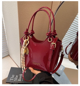 Detalle del bolso de charol rojo con asa de nudo y colgante de tenis en color dorado