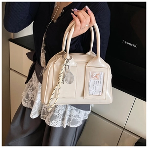 Detail of glossy beige top handle bag featuring a transparent card slot and tennis charm