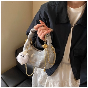 Détail d'un sac à main plissé argenté avec chaîne dorée et breloque en fourrure blanche