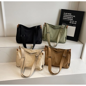 Detailed view of canvas tote bags in black, sage green, beige, and brown on marble