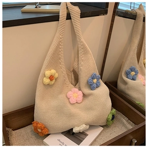 Close-up of beige knit tote bag with colorful 3D crochet flowers on a wooden tray