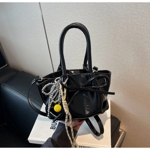Detail der schwarzen Lackleder-Beuteltasche mit Schleife und dekorativen Anhängern