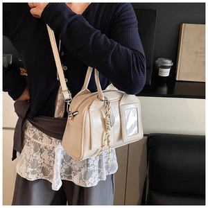 Close-up of beige crossbody pillow bag featuring a transparent card slot and woven pendant