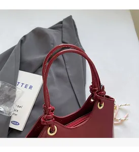 Detalle del bolso de charol rojo oscuro con asa anudada y herrajes metálicos dorados