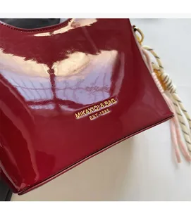 Detalle de bolso de charol rojo con logotipo dorado en relieve y textura de piel brillante