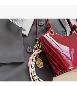 Detalle del bolso de charol burdeos con cuerda tejida blanca y colgante dorado