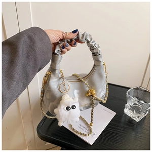 Détail du sac argenté métallisé avec poignée froncée, chaîne dorée et pompon blanc