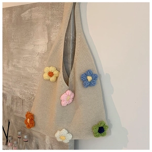 Detail of colorful 3D crochet flowers on a beige knit tote bag hanging on a wall