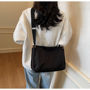 Detail of black canvas messenger bag with adjustable shoulder strap and side leather accent