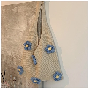 Detailed close-up of beige knitted tote bag with 3D blue floral crochet decorations