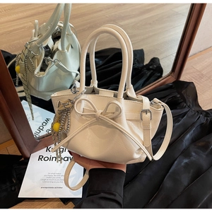 Detailsicht der beigen Rafftasche mit Schleifen-Design und silbernem Kettenanhänger