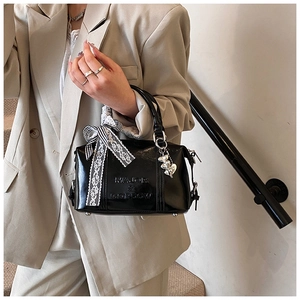 Close-up of black glossy Boston bag with lace bow and silver heart charm detail