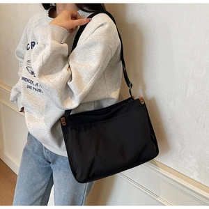 Close-up of black canvas crossbody bag featuring leather fasteners and adjustable strap