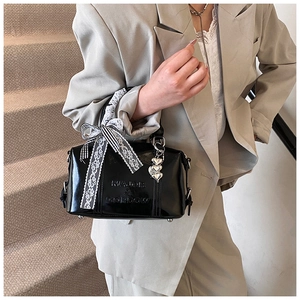 Detail of glossy black Boston bag featuring lace bow and metallic heart charms