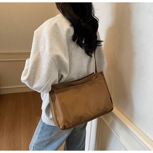 Brown nylon tote bag with large front pocket shown on shoulder in daily lifestyle