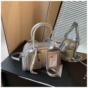 Detail of silver metallic Boston bag featuring a front pocket with card holder and charm