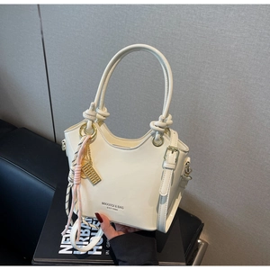 Detalle de bolso bucket de cuero crema con asas anudadas y colgantes dorados